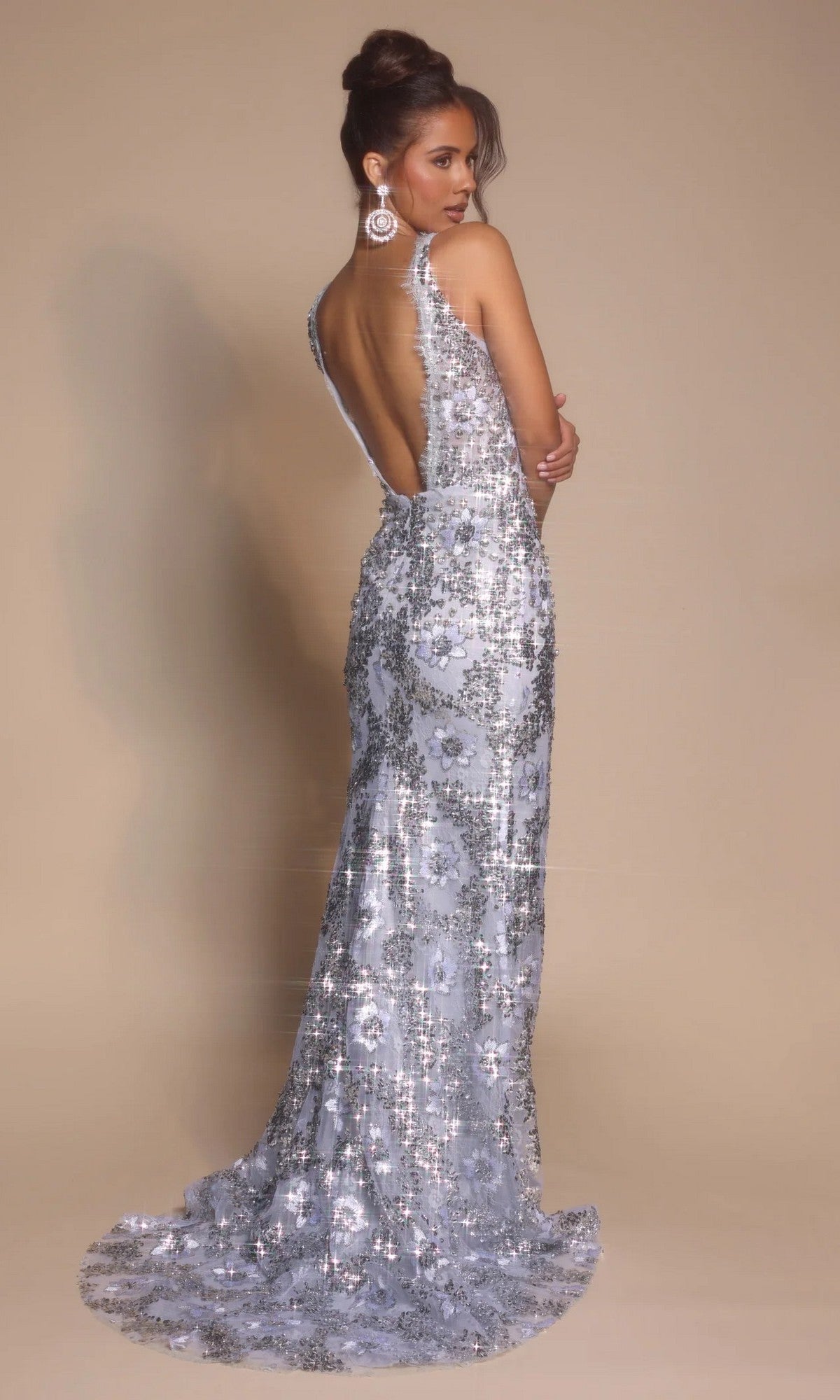 A woman poses in the Portia and Scarlett PS26043, a backless, floor-length formal dress with a sparkling finish and train, set against a beige backdrop.